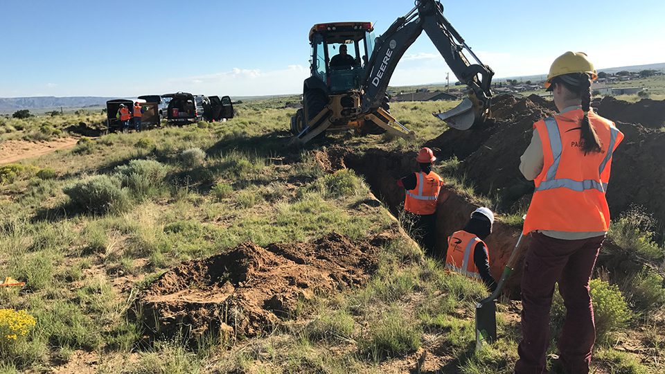 Woman in field taking notes next to digger truck.